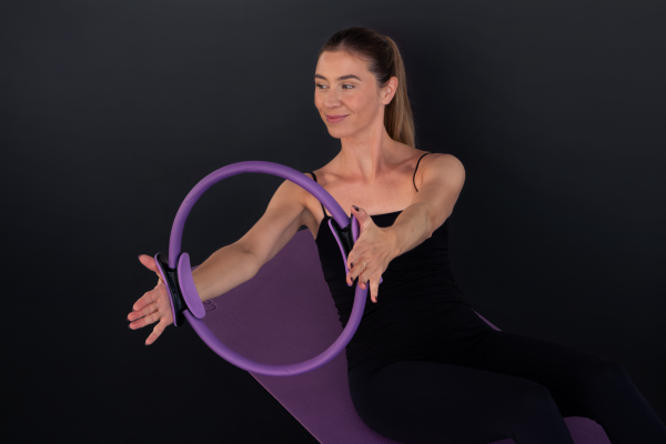 A woman doing a pilates exercise with a pilates ring on a mat